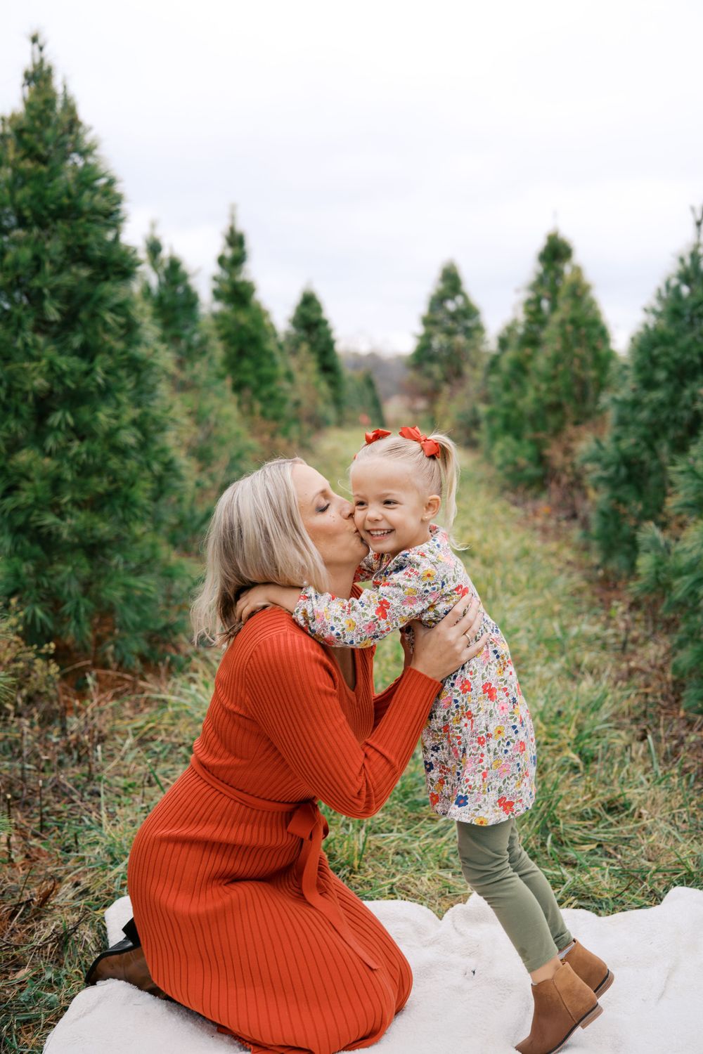 A tender moment shared between two people in a Christmas tree farm setting, wearing festive winter attire.