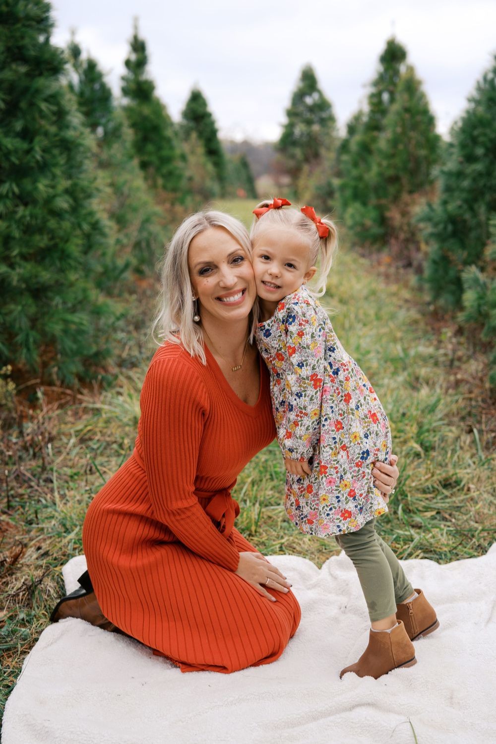 Sweet candid interactions on a white blanket among evergreen trees during a winter photo session.