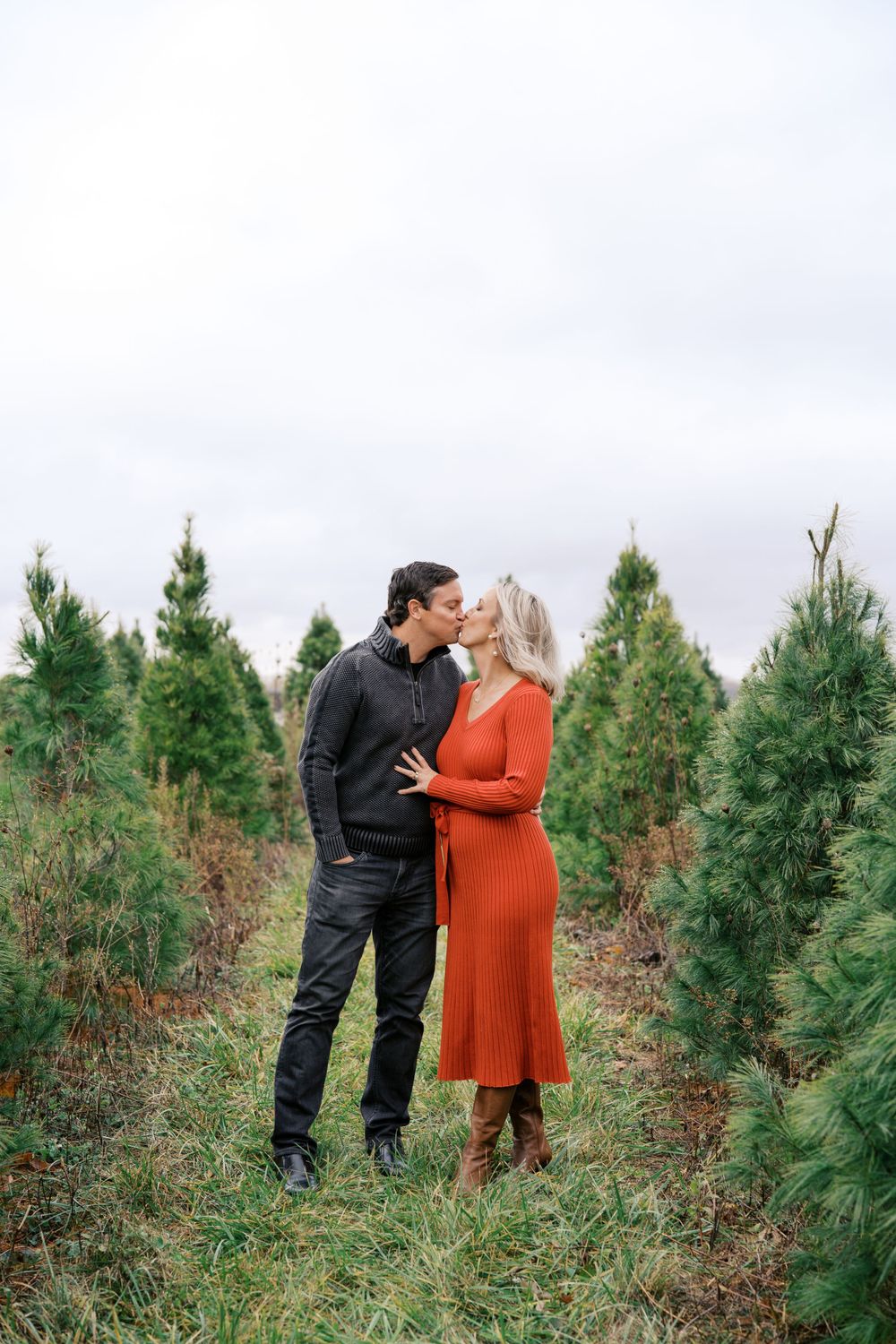 A couple embracing among evergreen trees, with one wearing a striking red dress.