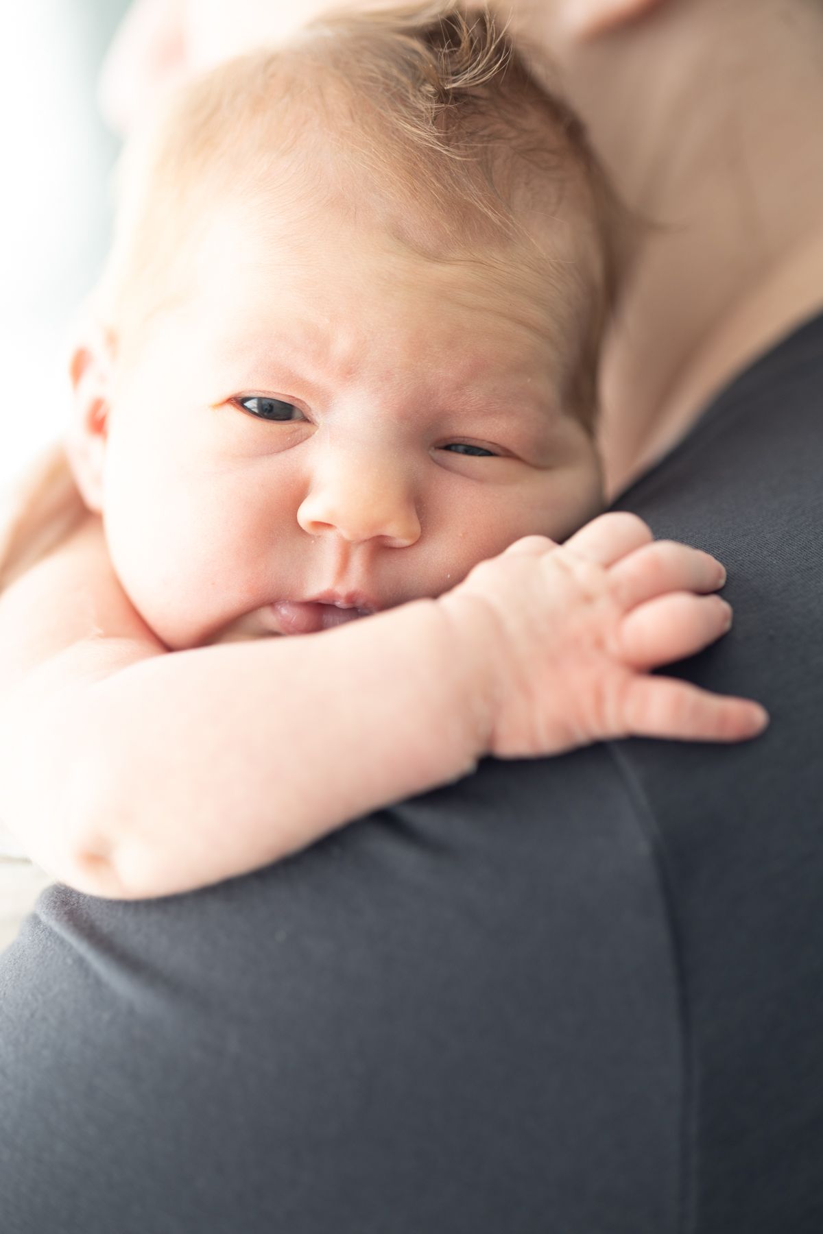 Newborn baby resting peacefully on parent's shoulder in soft lighting.