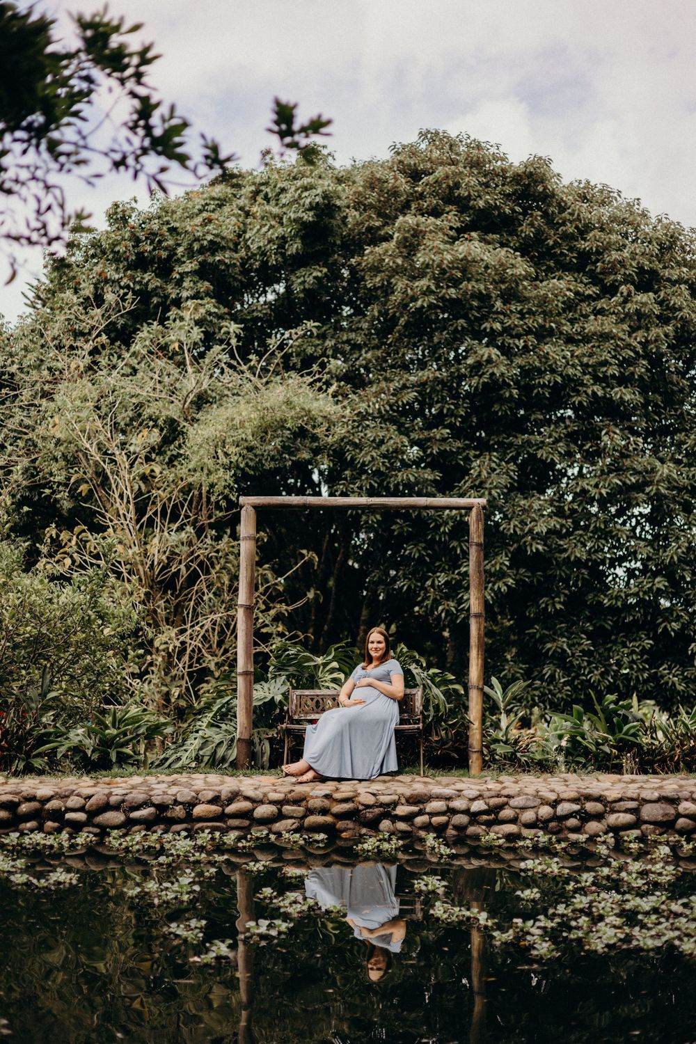 A wooden swing frame stands by a reflecting pool surrounded by lush tropical greenery.