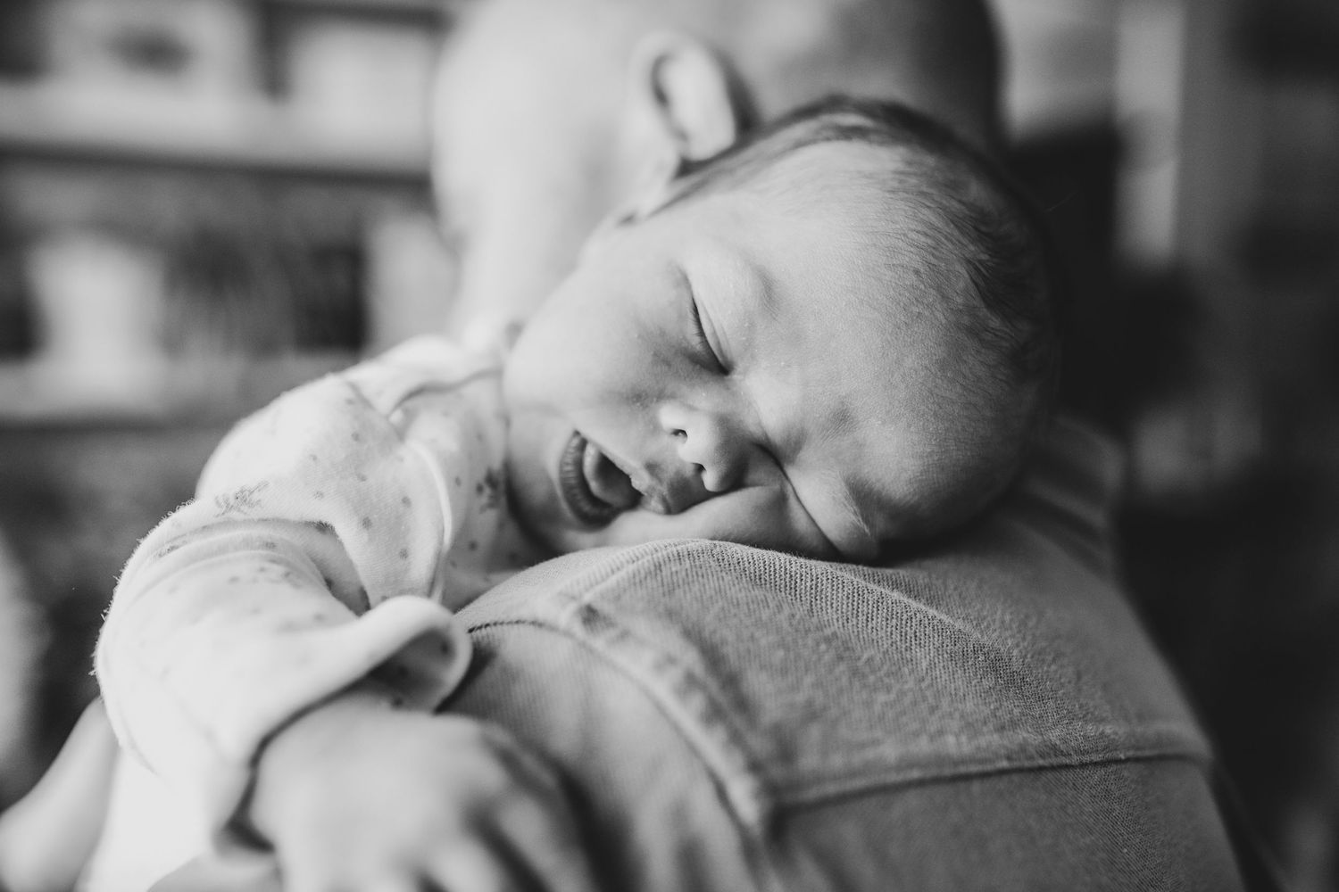 Black and white image of sleeping newborn resting on shoulder.