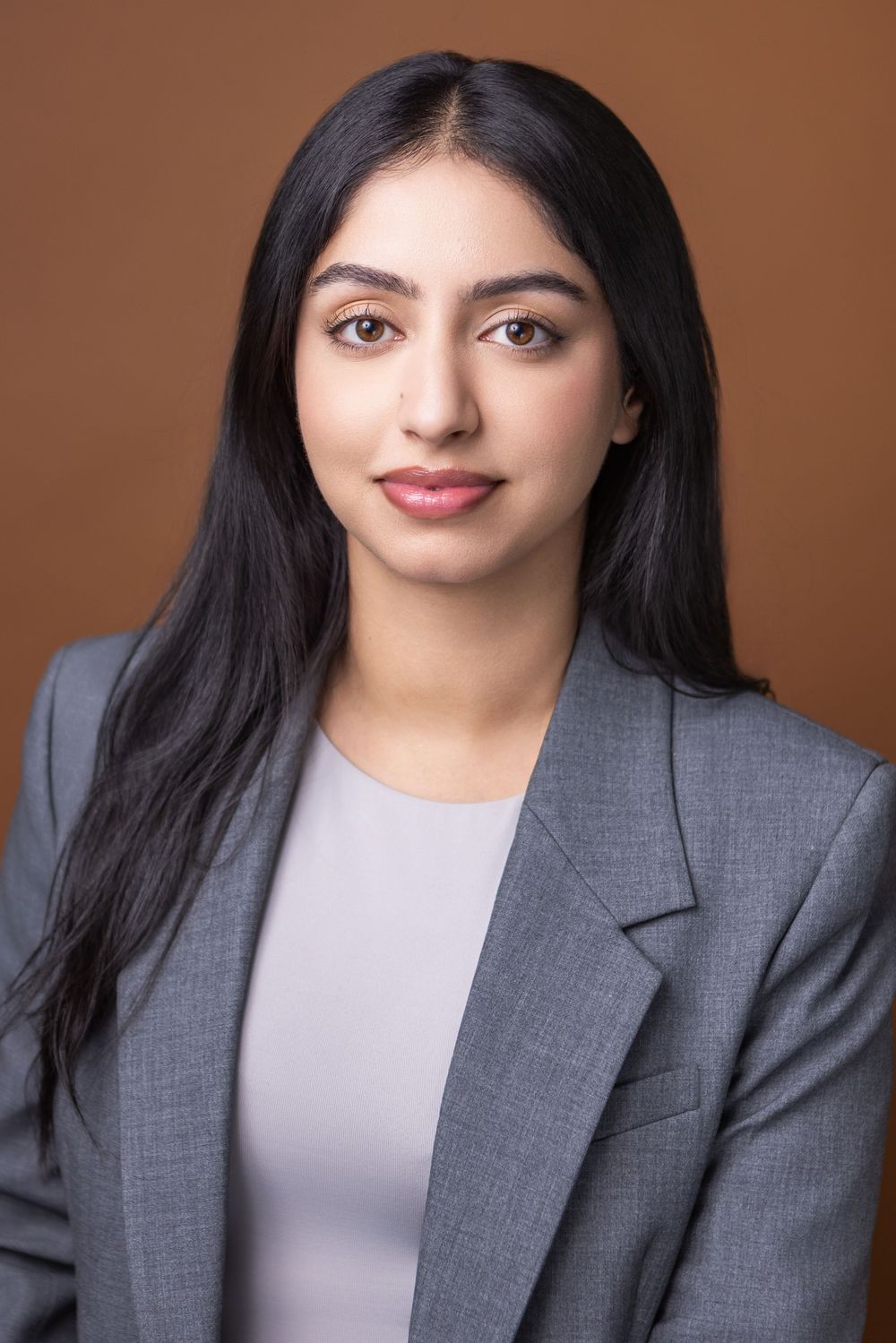 Professional headshot series showing different poses in a gray blazer and light top against a brown background.