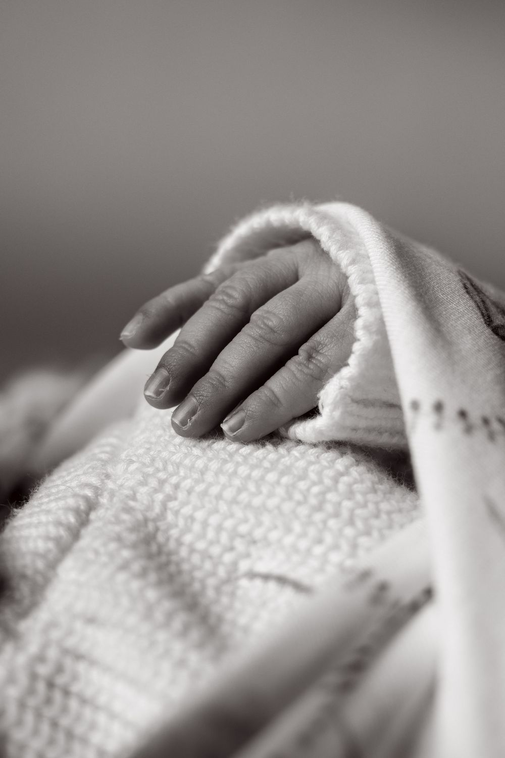 Close-up black and white photo of a newborn baby's tiny hand resting on a soft knit blanket.