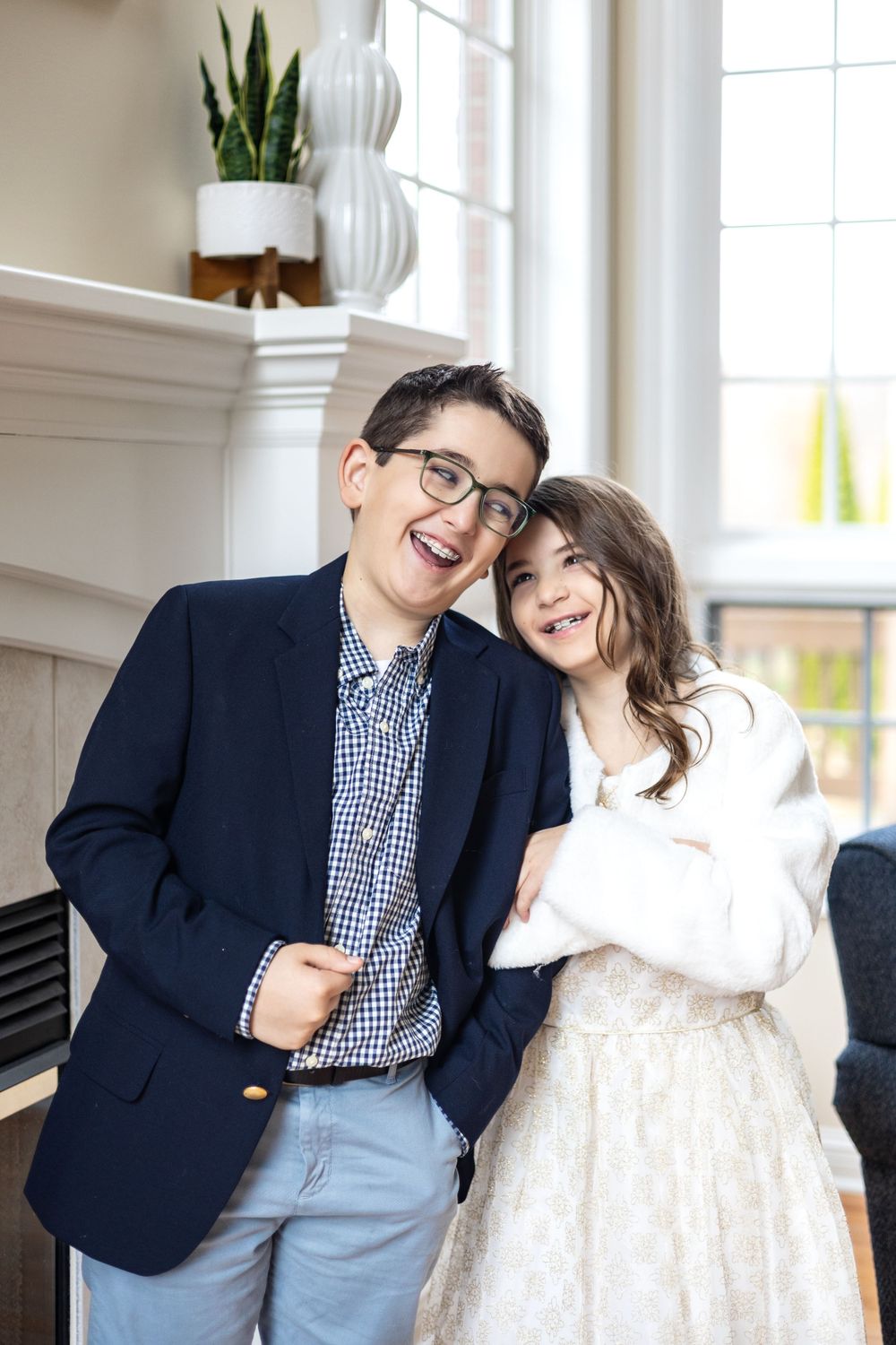 A happy couple in casual formal wear smile while posing together in a bright room with decorative houseplants.