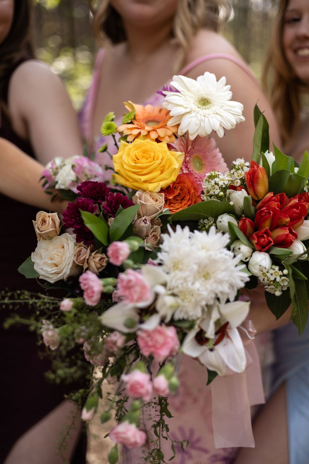 Vibrant wedding bouquet featuring white gerbera daisies, yellow roses, pink carnations and mixed flowers in natural outdoor setting.