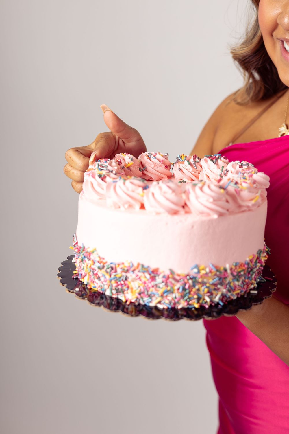 Pink frosted ice cream cake decorated with colorful sprinkles held at different angles showing vibrant details.
