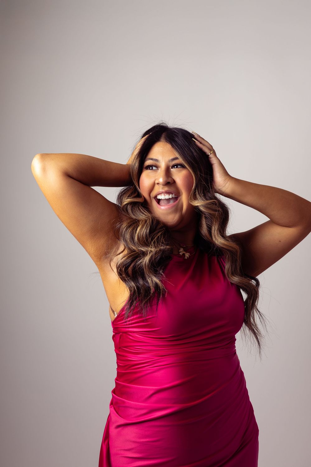 A person in a vibrant fuchsia top poses playfully against a neutral background with dynamic arm movements.