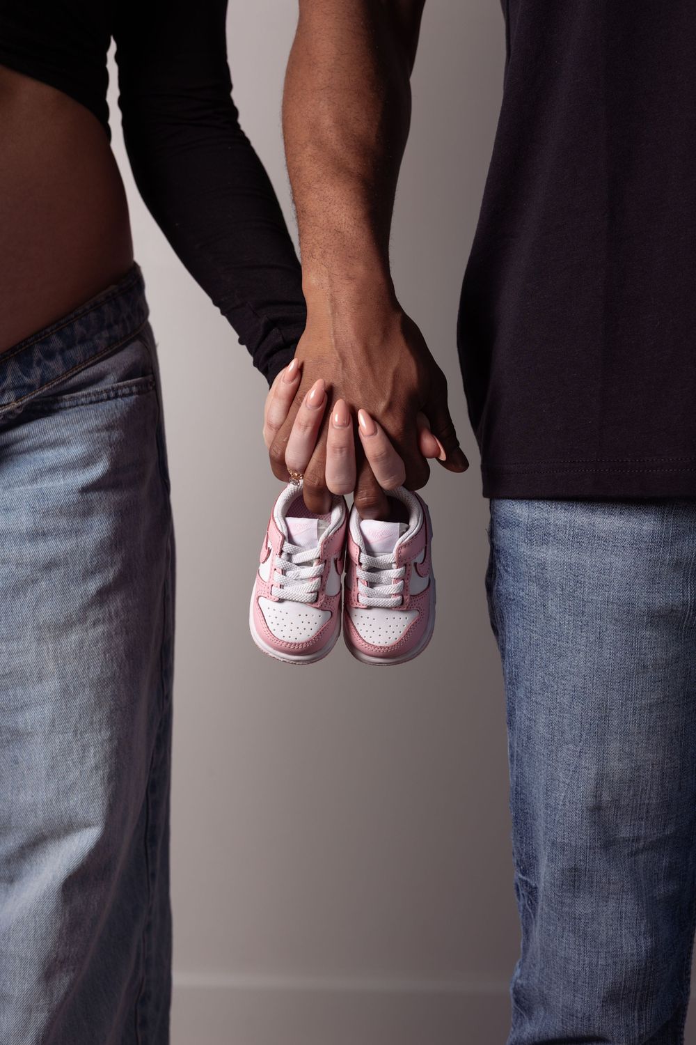 Couple holding tiny pink baby sneakers together, announcing pregnancy with adorable miniature shoes.