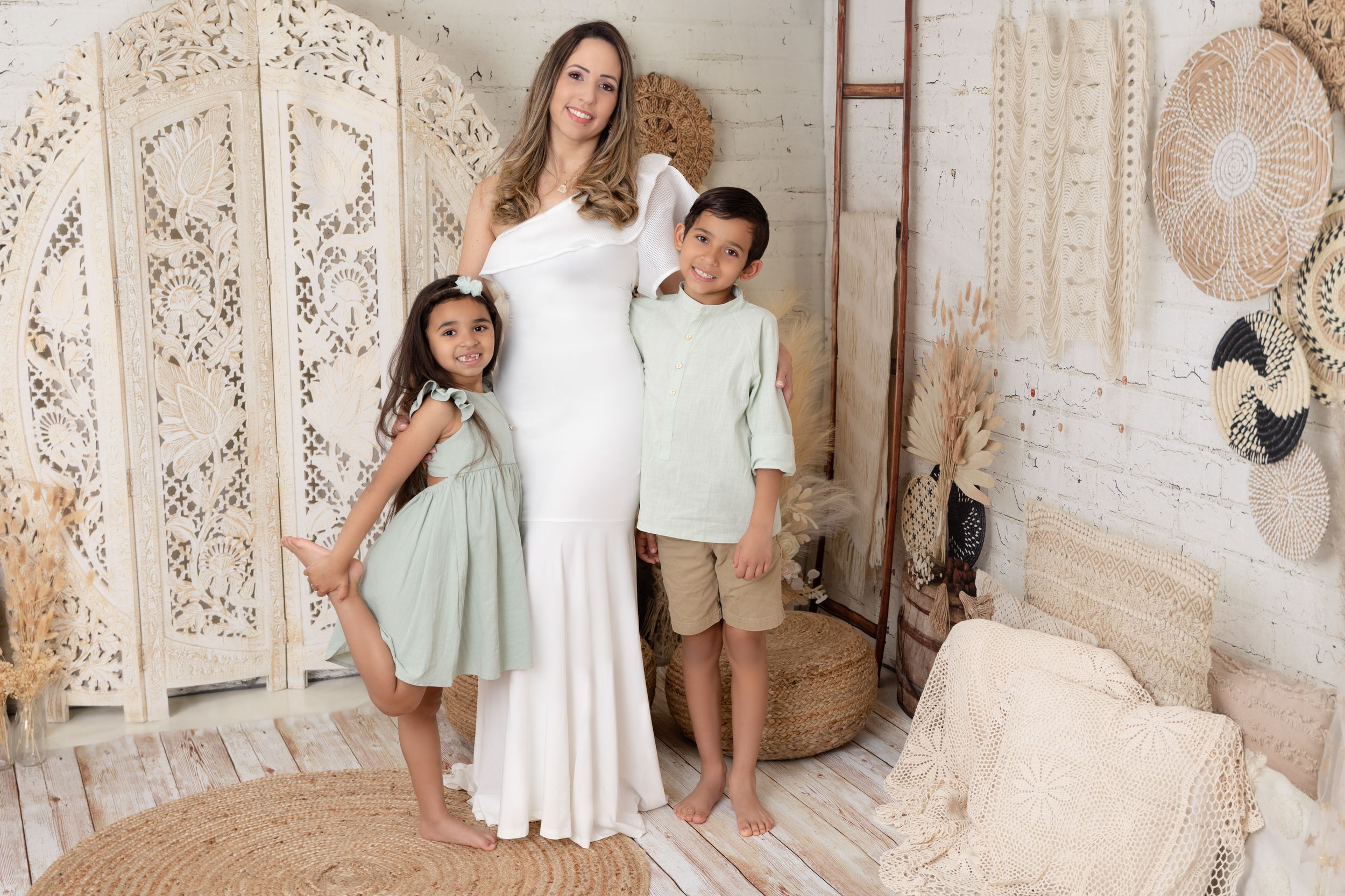 A family in coordinated neutral outfits poses together in a cozy boho-style room with decorative screens and woven decor.