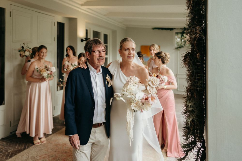 Wedding party in pink dresses and formal attire gather together in an elegant indoor setting.