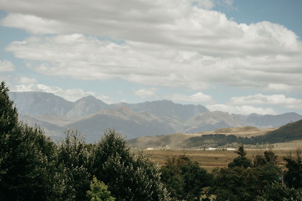 Mountain landscape with rolling hills and evergreen trees under cloudy blue skies.