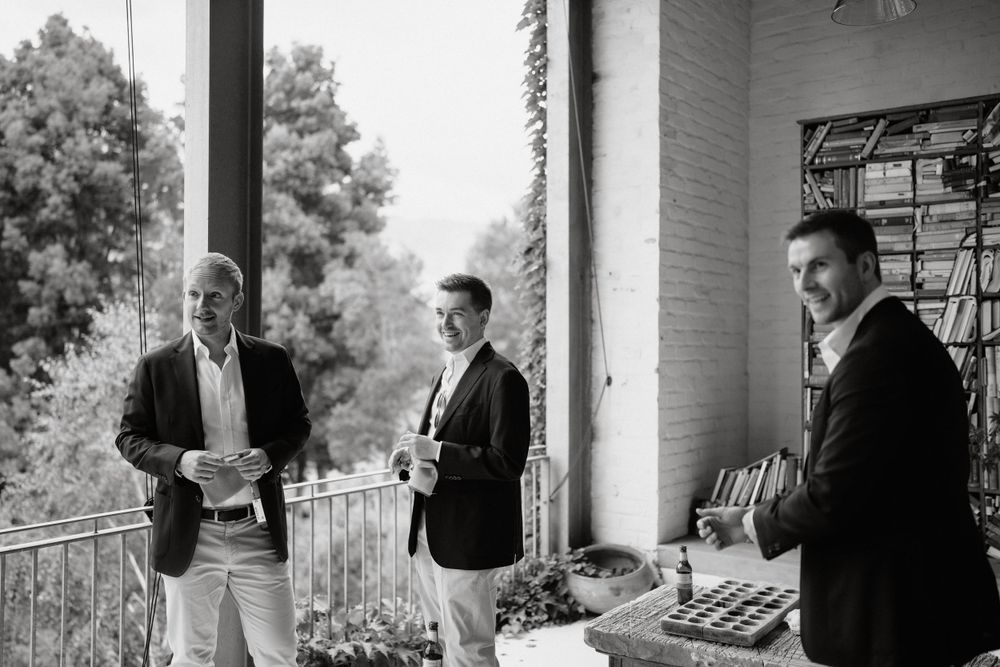 Men in formal attire gather on porch during pre-wedding preparations.