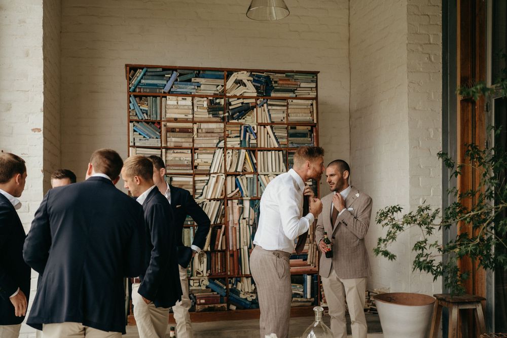 Wedding guests in formal attire gather and socialize in a bright indoor venue with artwork.