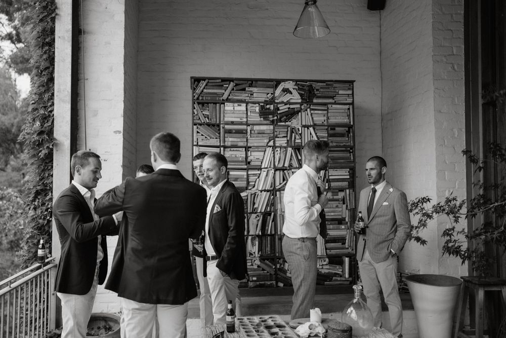 Groomsmen in traditional wedding attire gather on a porch before the ceremony.