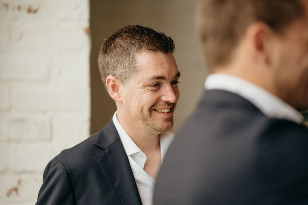 Candid moment showing man in dark suit smiling during wedding preparations.