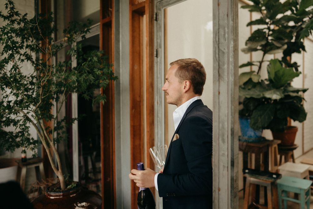 Person in navy suit standing near indoor plants by a window in natural light.