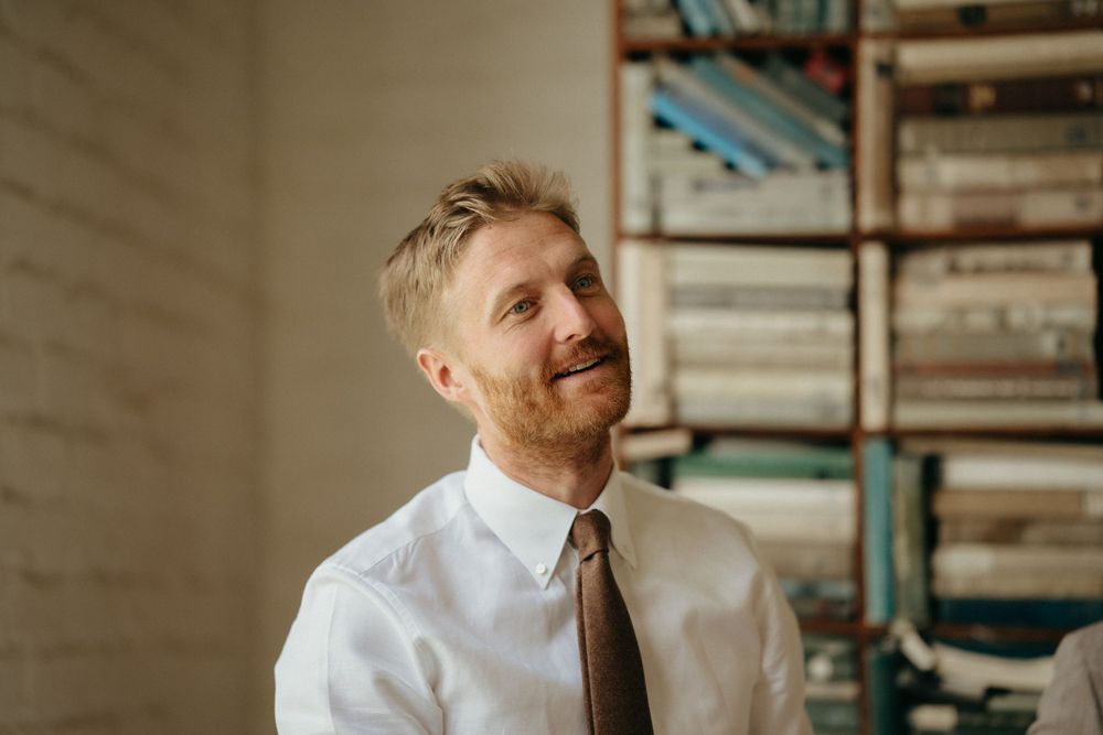 Groom in white shirt and tie smiles warmly against interior background with bookshelves.