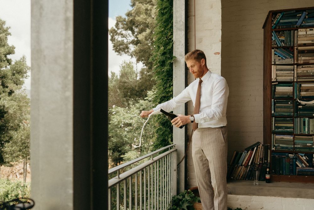 Person in white shirt and khaki pants stands on balcony surrounded by greenery.