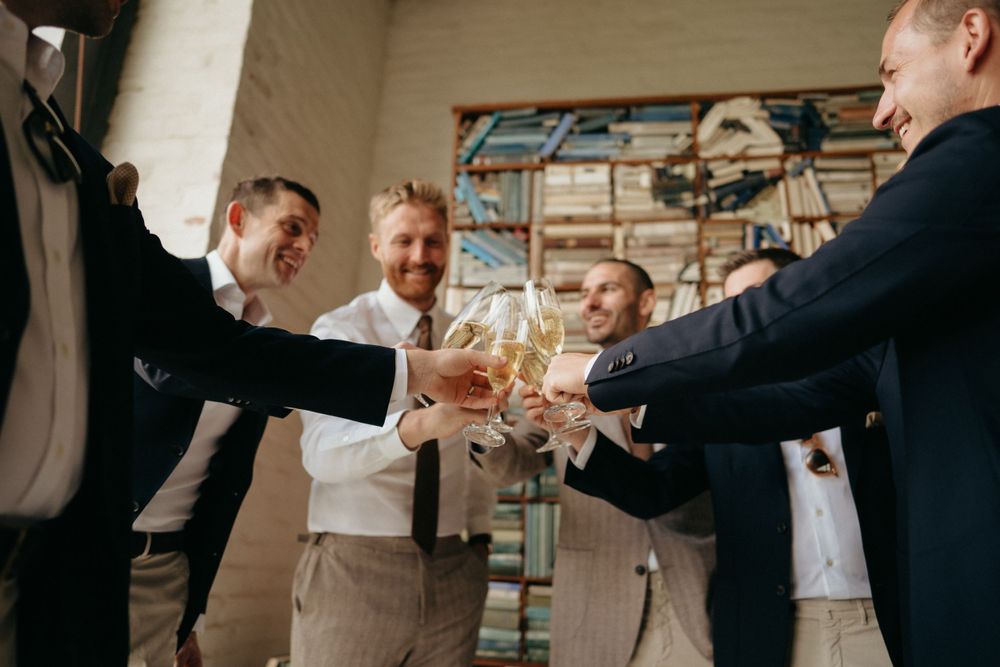 Group toasting with glasses during pre-wedding celebration near bookshelf wall.