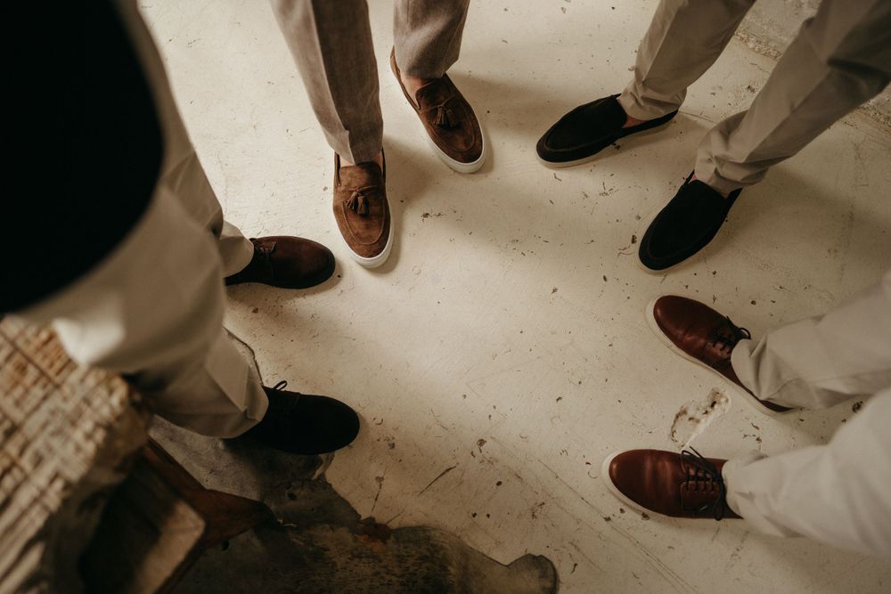 Artful detail shot of groomsmen's dress shoes arranged in a circle on light flooring.
