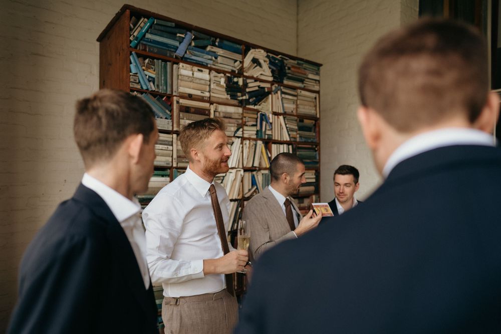 Groomsmen getting ready in casual attire against vintage bookshelf backdrop.
