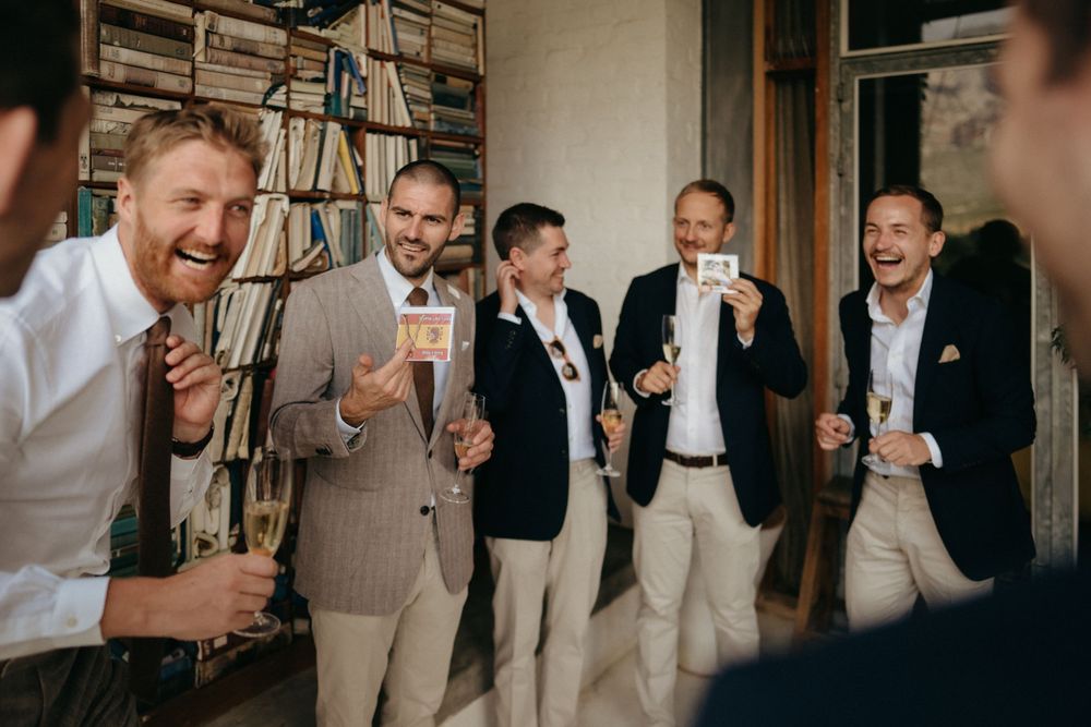 A group of groomsmen share drinks and laughter during a wedding celebration.