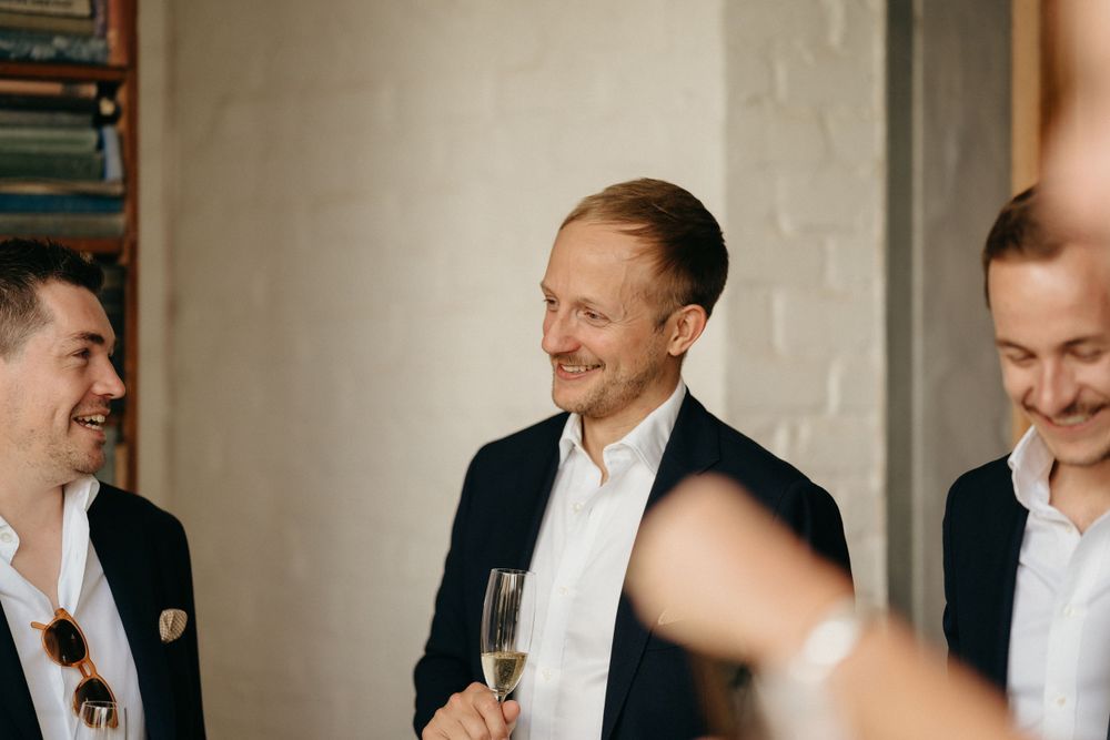 Three men in business attire share drinks and conversation at an indoor gathering.