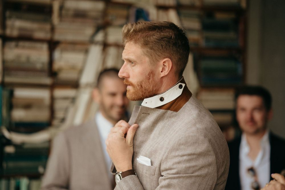 Groom adjusting tie while preparing with groomsmen in industrial-style room.