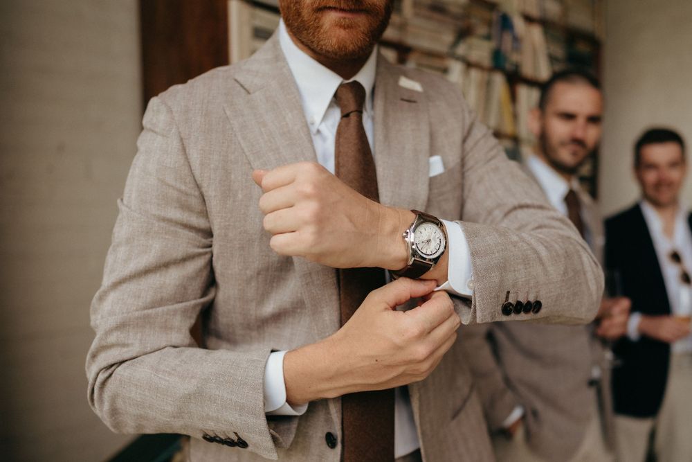 Close-up shot of groom adjusting watch while wearing light beige suit.