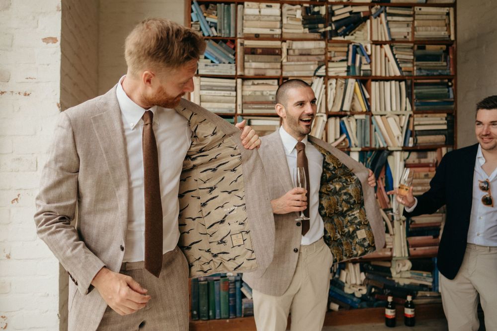 Groomsmen sharing laughs while getting dressed in beige and grey suits.