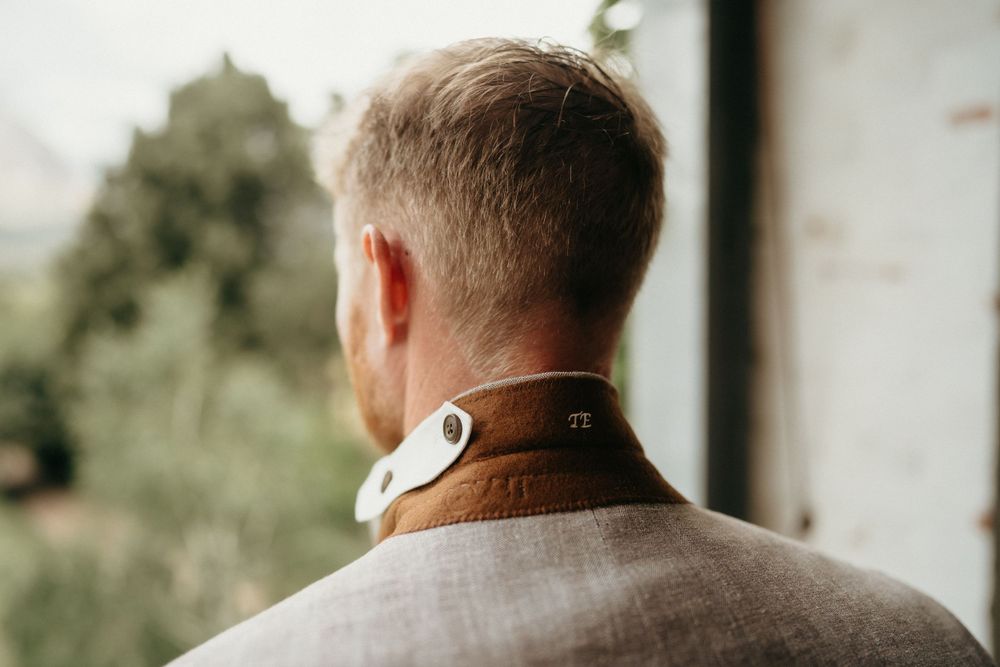 Back view of someone wearing a brown leather jacket and white collar in natural lighting.