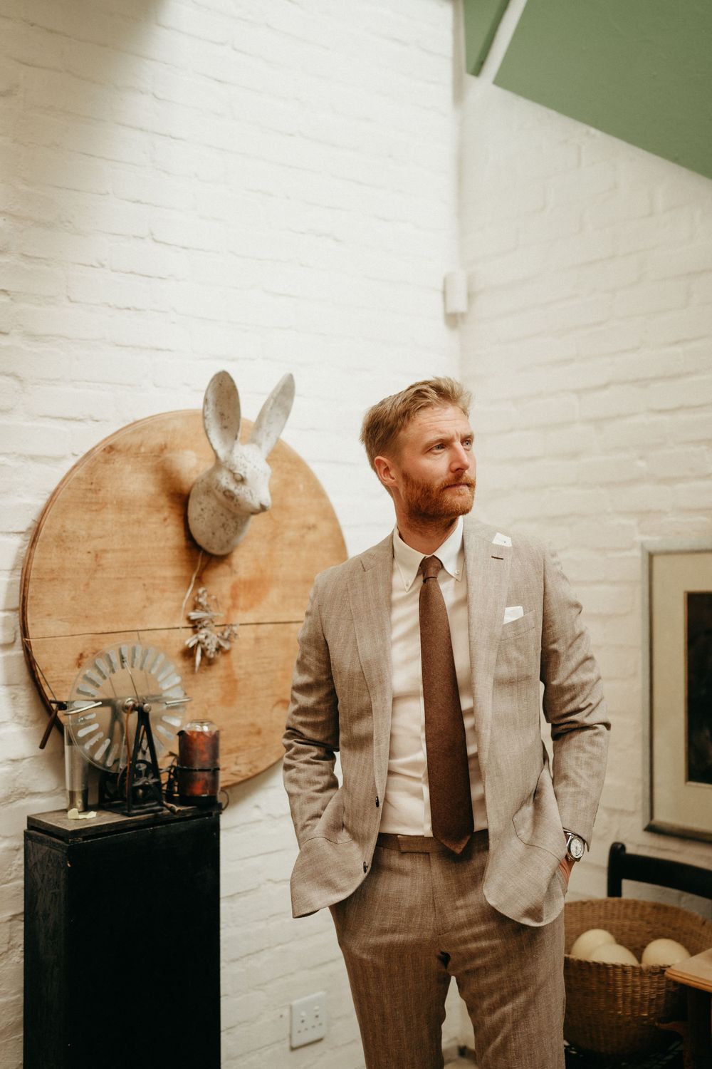 Modern wedding decor featuring beige suit against white brick wall with decorative rabbit art.