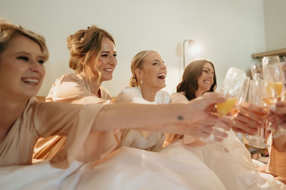 Friends raise glasses in celebration while wearing matching robes during pre-wedding preparations.