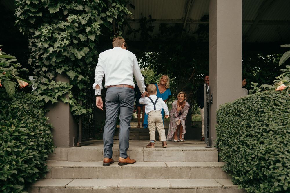 Adults and children walking up stone steps between manicured hedges.