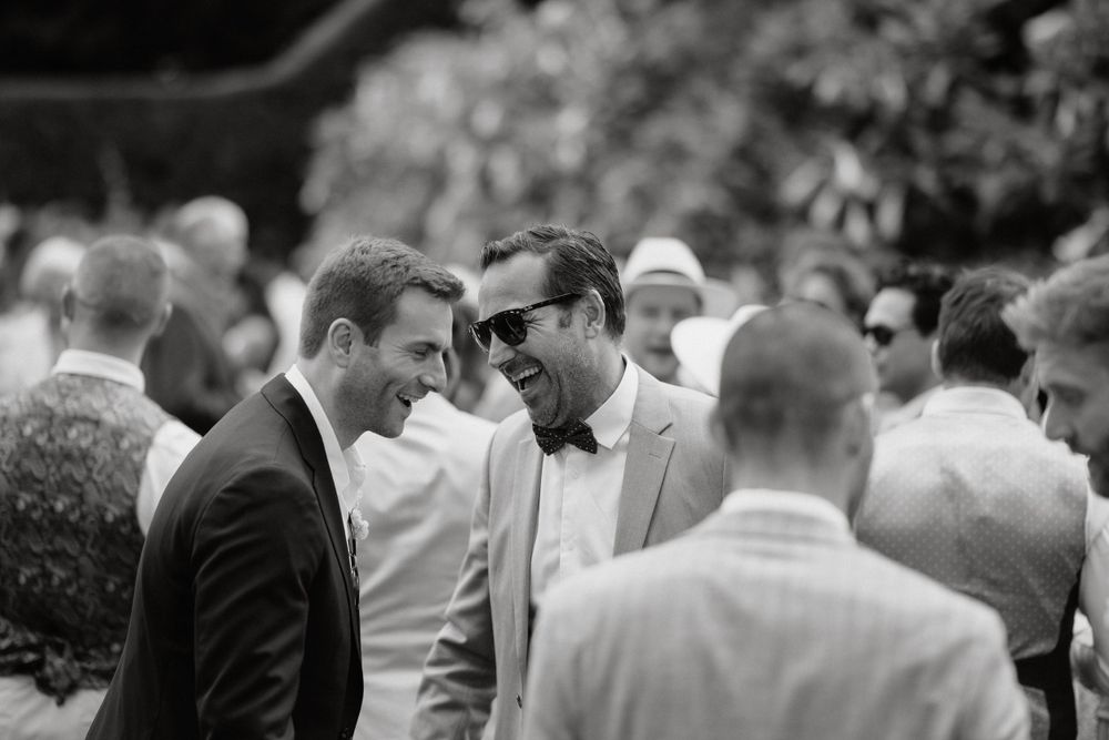 Two wedding guests in formal attire having an animated conversation during an outdoor reception.