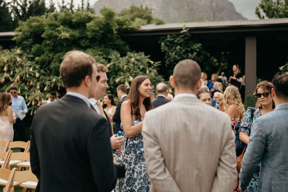 Outdoor wedding guests mingle and socialize during a daytime garden reception gathering.