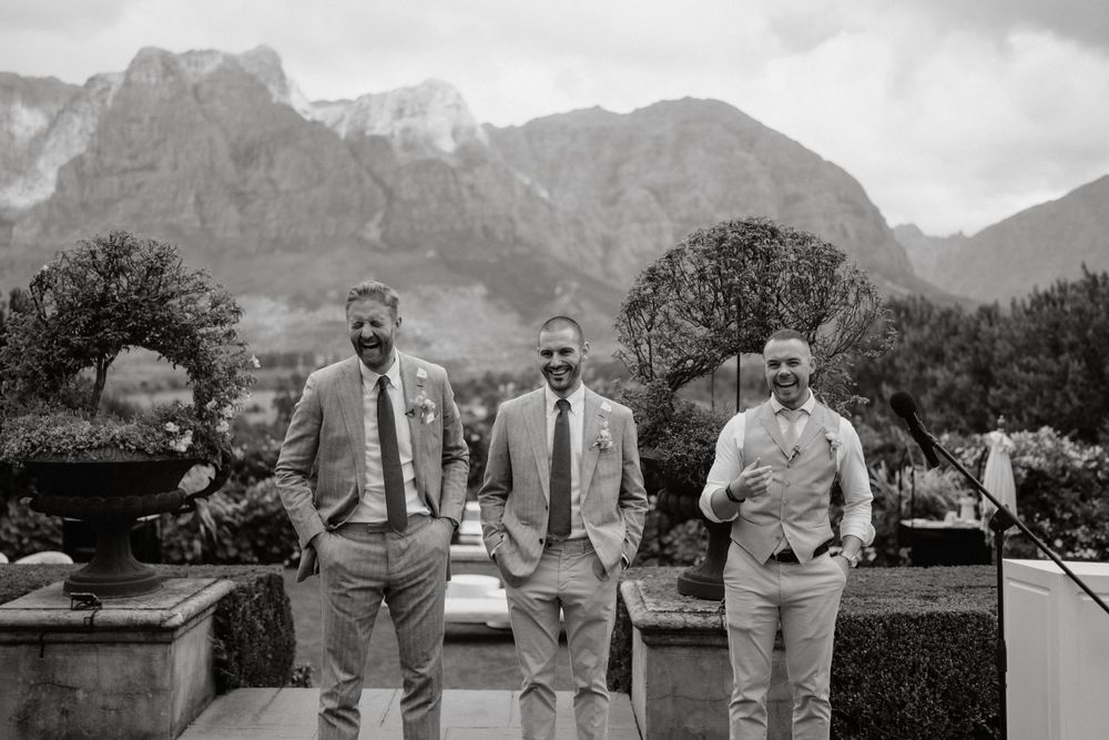 Three groomsmen pose against a backdrop of dramatic mountain peaks.