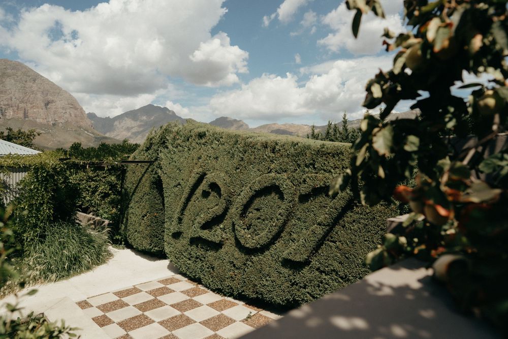 A hedge sculpture spells out '2021' against a mountainous landscape with fluffy white clouds.