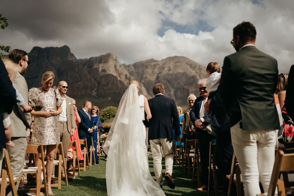 Wedding ceremony under cloudy skies with stunning mountain peaks in the background.