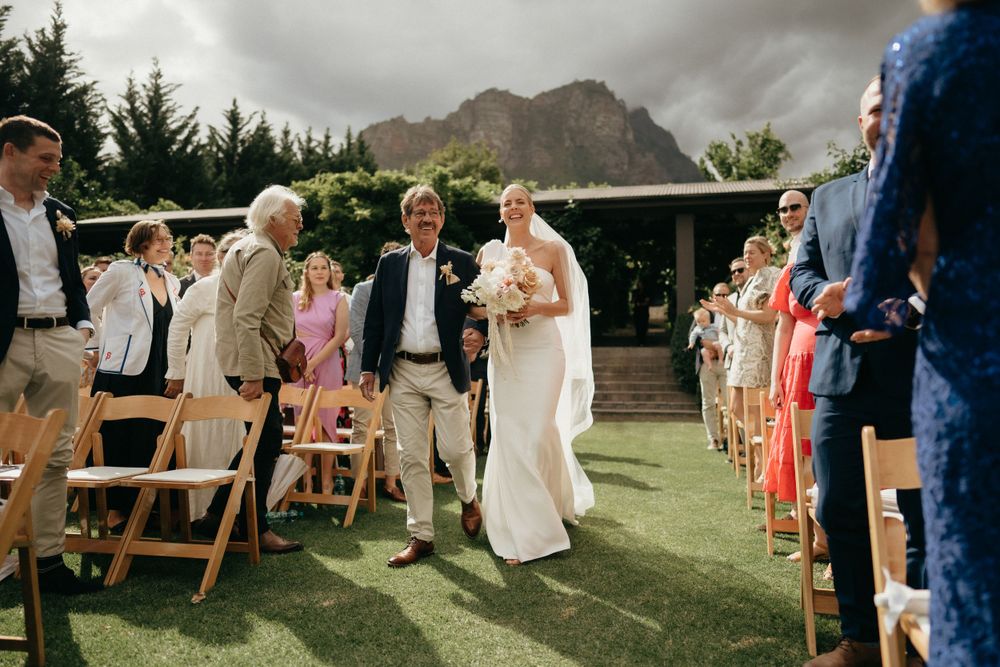 Outdoor wedding ceremony with mountain backdrop and wooden folding chairs on a manicured lawn.
