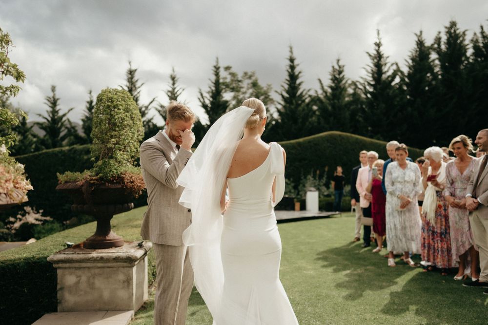 Newlyweds share their first dance on a manicured lawn surrounded by wedding guests.