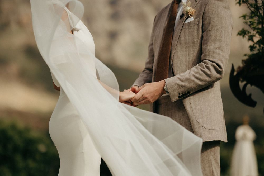 Close-up of flowing white wedding dress fabric being held against a tan suit.