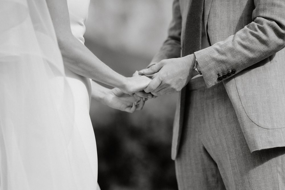 Black and white closeup of couple holding hands during wedding ceremony exchange.