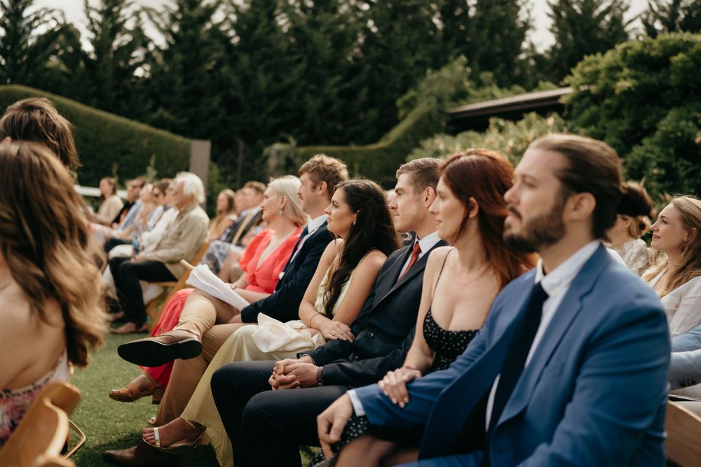 Wedding guests seated in rows on a garden lawn during an outdoor ceremony.