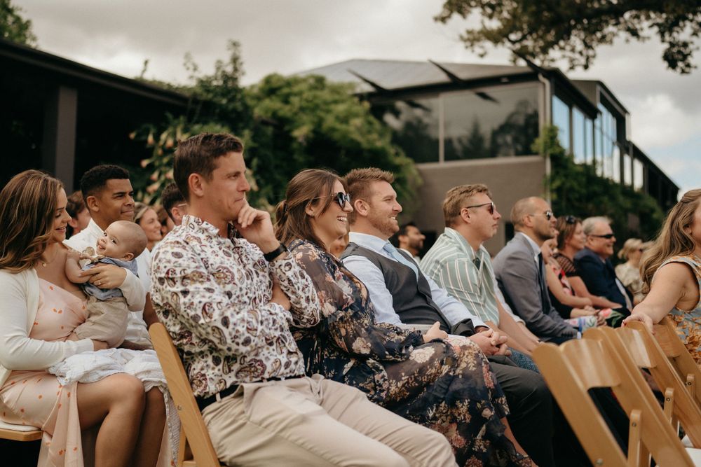 Wedding guests seated on wooden chairs during an outdoor ceremony with mountain scenery in the background.