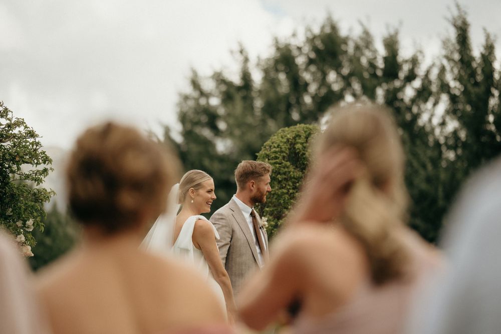 Intimate outdoor wedding ceremony with guests looking on against mountain landscape.