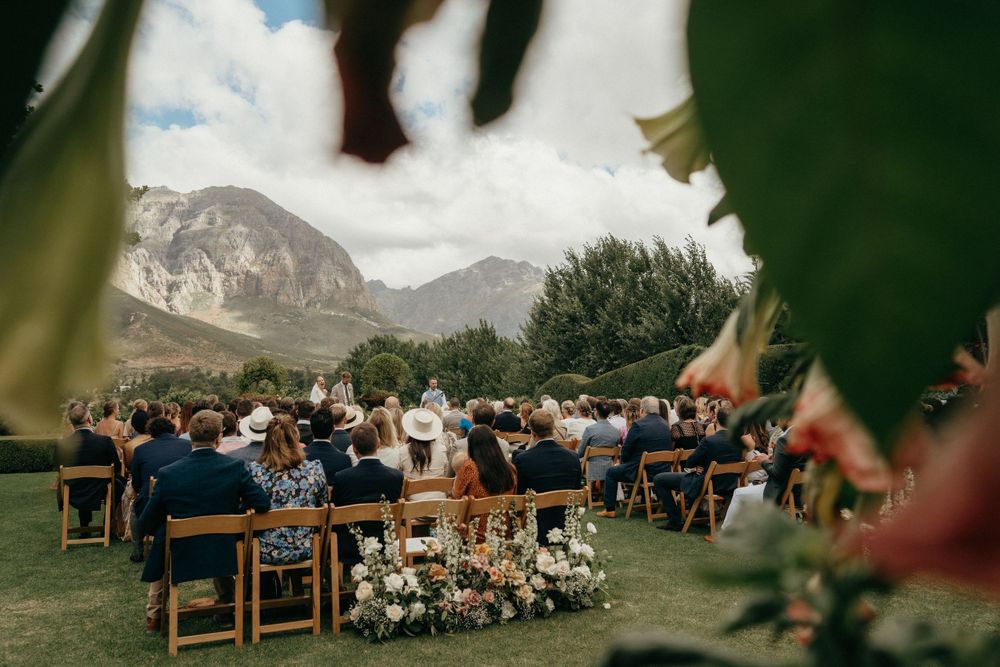 Outdoor wedding guests seated with mountains and blue sky create a scenic ceremony backdrop.