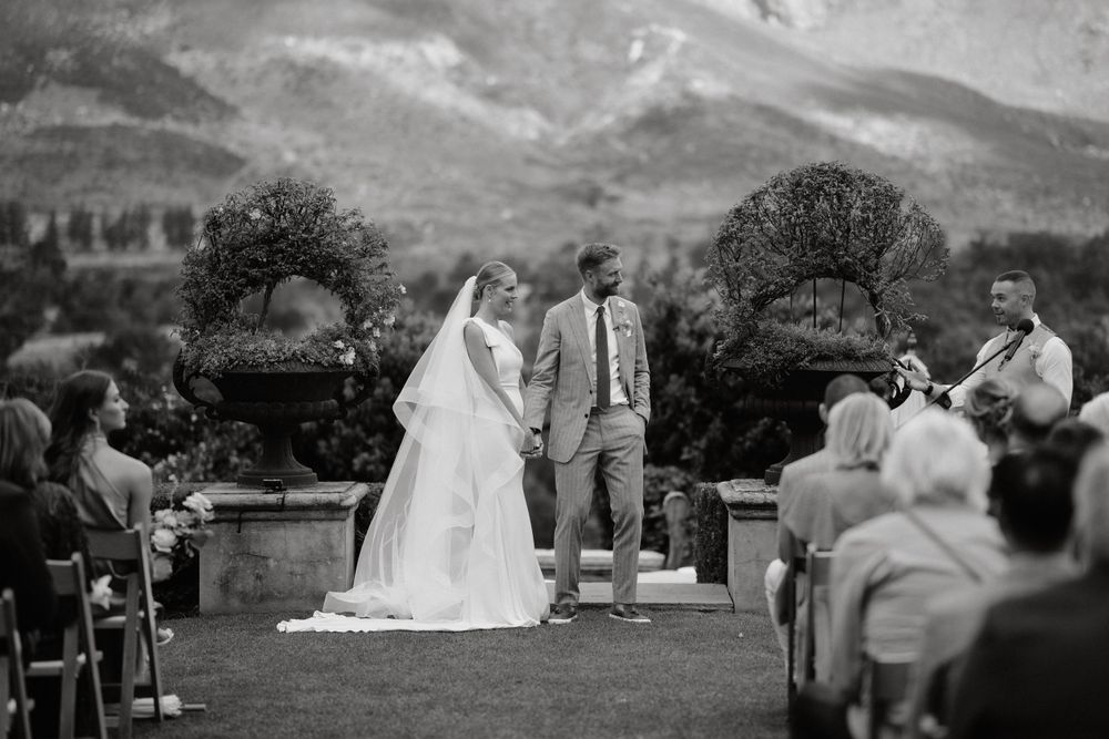 Black and white photo of a wedding ceremony against a scenic mountain backdrop with seated guests.
