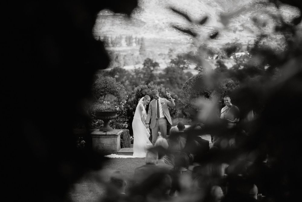 Artistic black and white photo of a wedding ceremony through foliage.